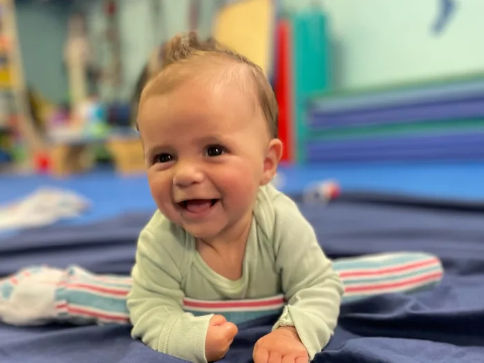 Smiling baby doing tummy time on a therapy mat