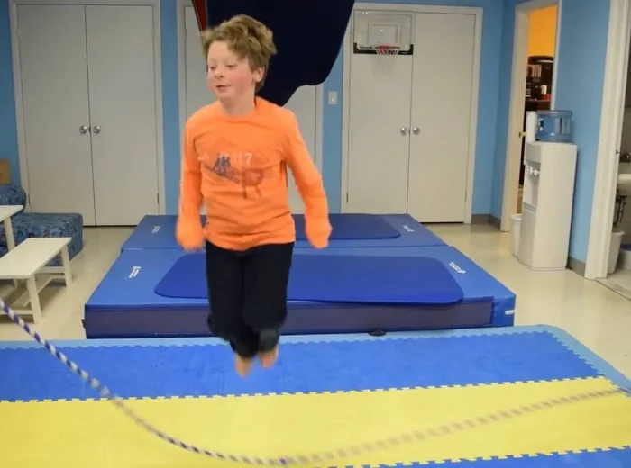 School age boy jumping rope on the mats in the therapy gym