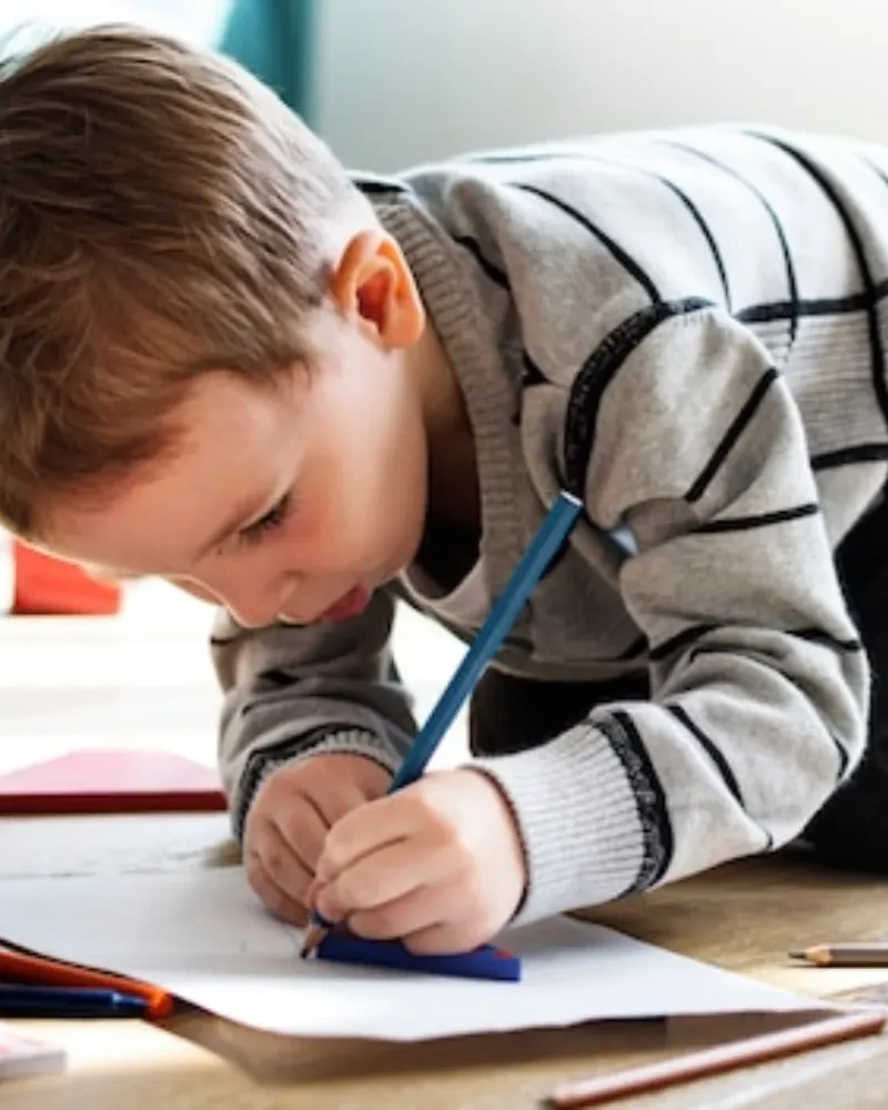 School age boy kneeling on the floor drawing with a blue pencil
