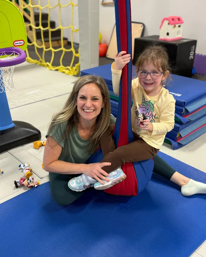 Pediatric therapist sitting with a smiling young girl on a therapy swing at Developmental Steps