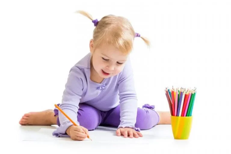 Young girl sitting on the floor drawing with a colored pencil next to a cup of pencils