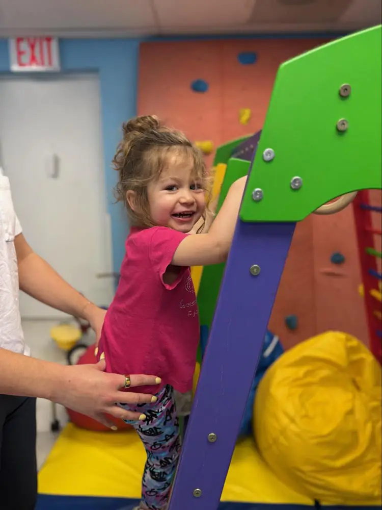 Young girl climbing a play structure in the therapy gym