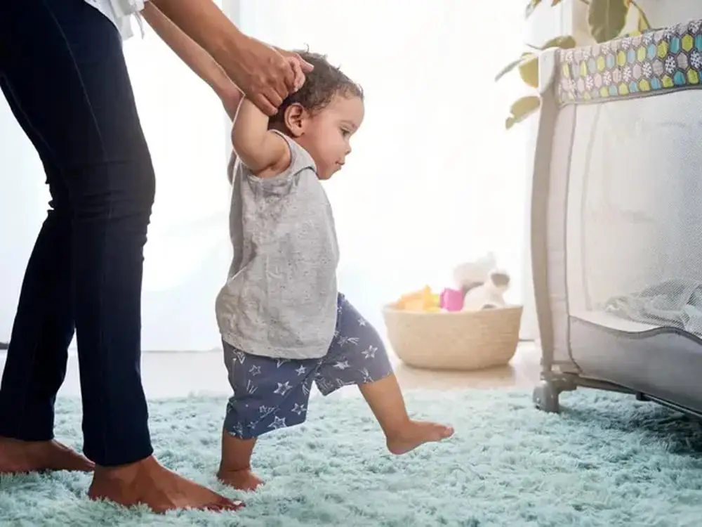Toddler taking first steps while a parent holds his hands