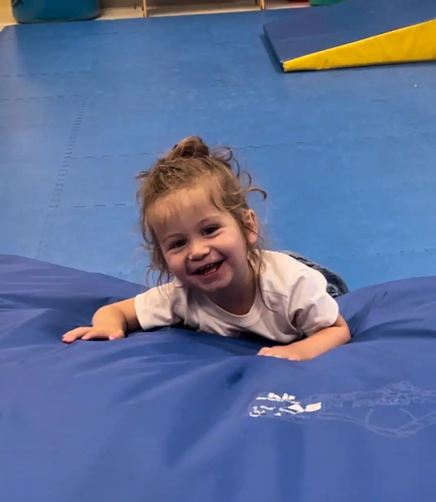 Smiling toddler pushing up on her arms on a therapy mat