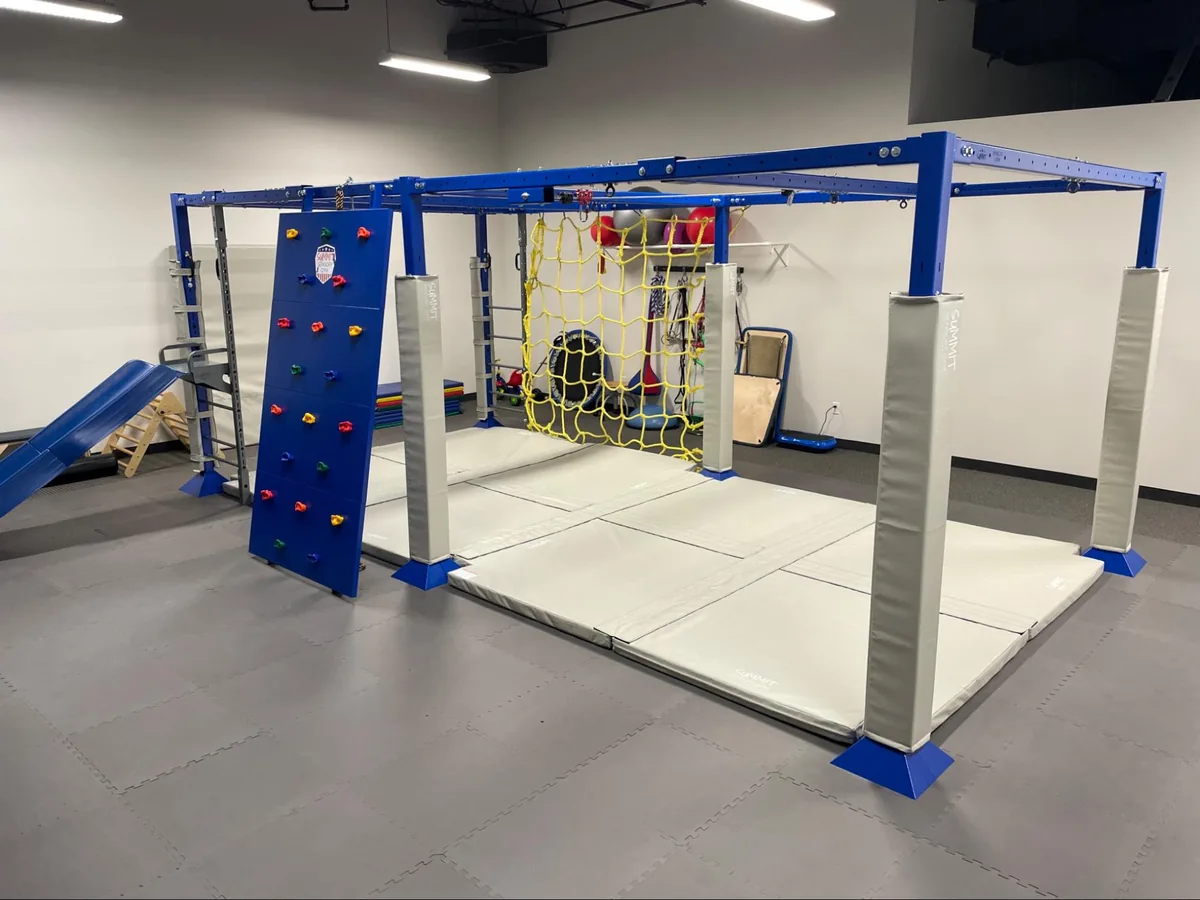 The Mt Kisco therapy gym with a blue climbing frame, rock wall and yellow climbing net